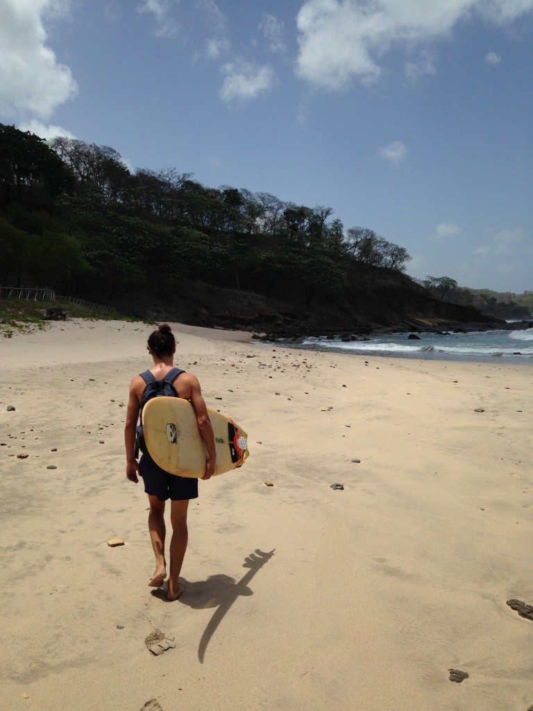 Andrés caminando por la playa con una tabla de surf en la mano