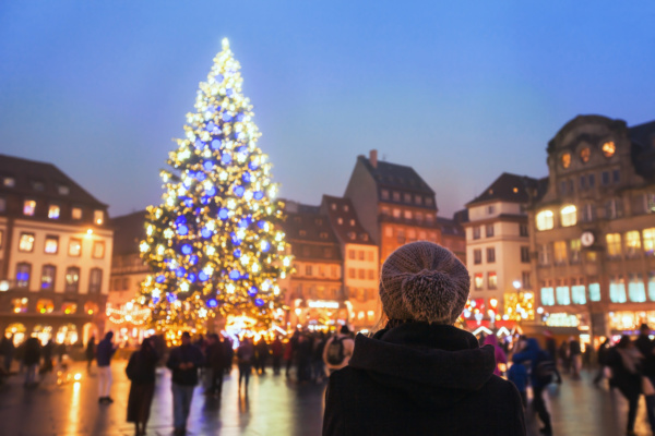 people in christmas market, woman looking at the decorated illuminated tree, festive new year lights in Strasbourg, France, Europe